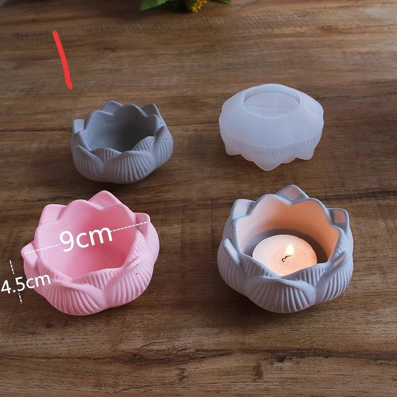 May include: Four lotus flower shaped candle holders, two are gray and two are pink. One gray holder has a lit tea candle inside. The pink holder has measurements of 4.5 cm and 9 cm.