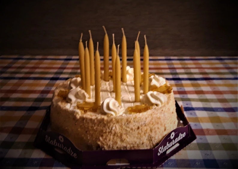 Op de afbeelding: Een ronde cake met witte frosting en verschillende toppings, waaronder karamel en slagroom. De cake is versierd met 15 gele kaarsen.