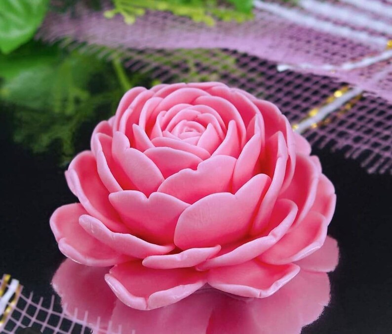 May include: A single, large, pink rose made of soap. The rose is in focus and the background is blurred.