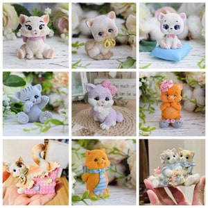May include: Nine different handmade ceramic cat figurines in various poses and colors. The cats are wearing accessories like bows, collars, and scarves. Some of the cats are sitting, while others are standing or lying down.