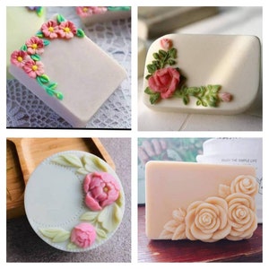 Puede incluir: Cuatro barras de jabón diferentes con diseños florales. Los jabones son de color blanco, verde claro y melocotón claro. Los diseños florales están hechos con jabón rosa, blanco y verde. Todos los jabones son rectangulares excepto uno que es redondo.