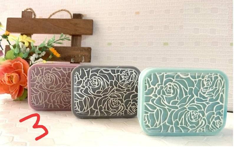 K&ouml;nnte beinhalten: Drei rechteckige Plastikbeh&auml;lter mit Blumendesigns. Die Beh&auml;lter sind in den Farben Rosa, Grau und Hellblau. Das Blumendesign ist ein sich wiederholendes Muster aus Rosen.