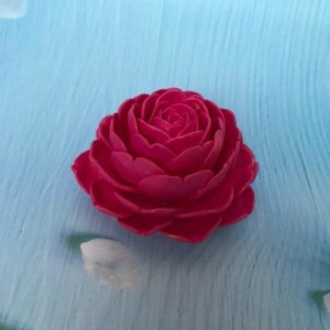 May include: A single, bright pink, artificial rose flower with multiple layers of petals. The rose is on a blue background.