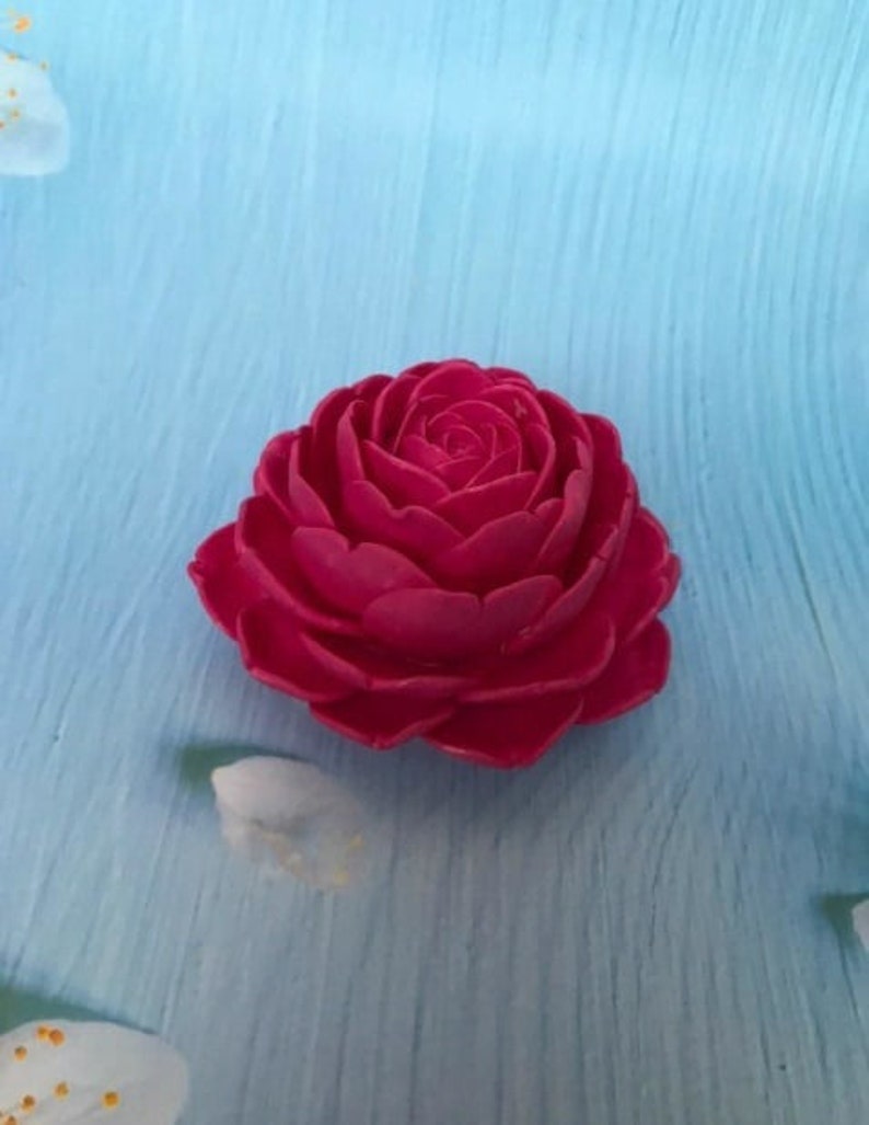 May include: A single, bright pink, artificial rose flower with multiple layers of petals. The rose is on a blue background.