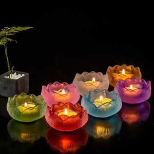 May include: Eight lotus-shaped candle holders in various colors, including pink, purple, blue, green, and red. Each holder has a small candle inside, creating a warm glow.
