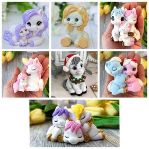 May include: A selection of handcrafted pony figurines in shades of white, purple, pink, and blue. Some ponies feature festive details such as a Santa hat and a wreath. The figurines show ponies in pairs or groups, frequently in a cuddling pose.