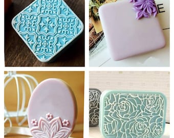 May include: Four different silicone soap molds. The first mold is square and features a blue and white geometric pattern. The second mold is square and features a light purple color. The third mold is oval and features a light purple color. The fourth mold is rectangular and features a blue and white floral pattern.