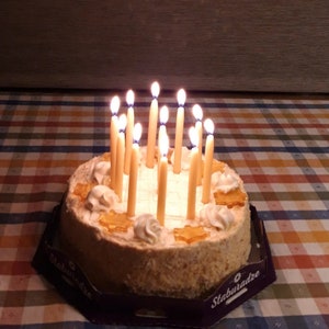 Op de afbeelding: Een ronde cake met witte frosting en verschillende toppings, waaronder karamel en noten. De cake is versierd met 18 brandende kaarsen.