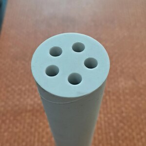 Puede incluir: Un cilindro de cer&aacute;mica blanco con cuatro agujeros en la parte superior. El cilindro est&aacute; sobre una superficie de madera marr&oacute;n.