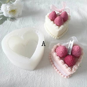 May include: A white silicone heart-shaped mold with a pink heart-shaped cake with white frosting and three red strawberries on top. The cake is decorated with white pearls around the edge. The cake is labeled "Handmade Especially for You".