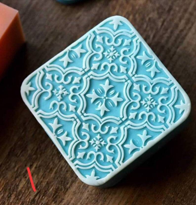 K&ouml;nnte beinhalten: Eine quadratische, hellblaue Seife mit einem wei&szlig;en, komplizierten, geometrischen Muster. Die Seife hat ein erhabenes Design.