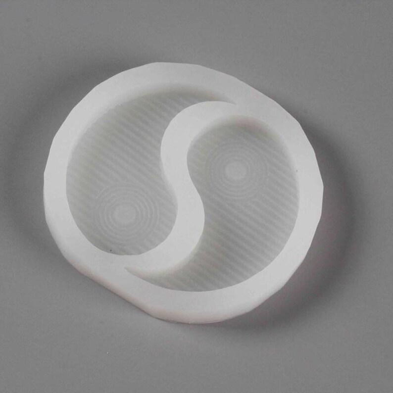 May include: White silicone mould shaped like a yin yang symbol. The mould has two separate compartments, each with a textured surface.