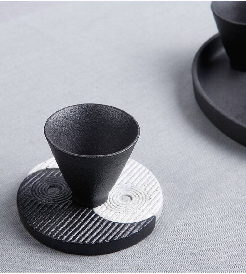 May include: Black and white ceramic teacup and saucer set with a yin yang design. The saucer is round with a black and white yin yang design. The teacup is black and sits on top of the saucer.