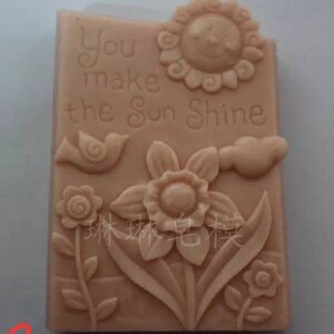 May include: A light brown rectangular soap mold with a raised design of a sun, a bird, a flower, and the text "You make the sun shine".
