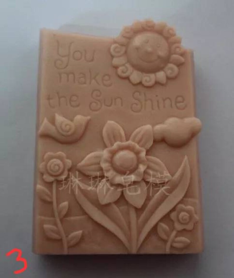 May include: A light brown rectangular soap mold with a raised design of a sun, a bird, a flower, and the text "You make the sun shine".