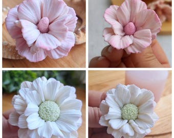 May include: Four handmade flower decorations. Two are light pink with a darker pink edge and a pink center. The other two are white with a light green center. All have multiple layers of petals.