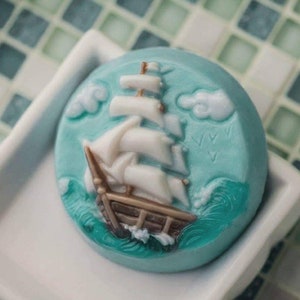 Op de afbeelding: Een ronde, blauwe zeep met een wit zeilbootontwerp. De zeilboot heeft bruine zeilen en vaart op een blauwe zee met witte wolken.