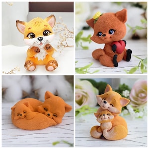 Könnte beinhalten: Eine Sammlung von vier Fuchsstatuen. Eine sitzt, eine andere hält ein Herz, eine dritte ist mit einem kleineren Fuchs zusammengerollt, und die letzte hat einen kleineren Fuchs in ihren Armen. Die Füchse sind orange und hellbraun mit detaillierten Merkmalen.