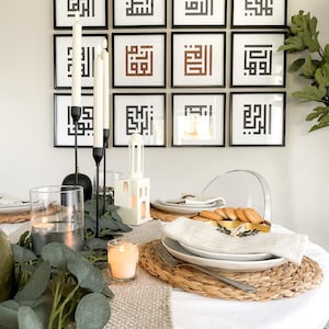 Puede incluir: Un mantel blanco con un camino de mesa beige y un mantel individual tejido. Un plato blanco con una servilleta blanca y un tenedor dorado est&aacute; sobre el mantel individual. Hay velas y vegetaci&oacute;n en la mesa. Un portavelas de cer&aacute;mica blanca con forma de casa est&aacute; sobre la mesa. Hay 12 impresiones enmarcadas en blanco y negro en la pared detr&aacute;s de la mesa.