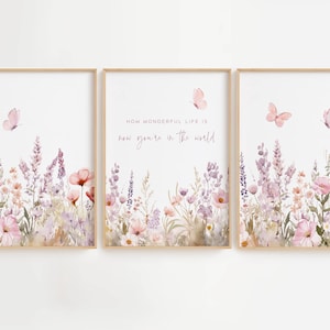 May include: Set of three framed art prints featuring watercolor illustrations of wildflowers in shades of pink, purple, and white. Pink butterflies flutter above the floral arrangements. The center print includes the text: "How wonderful life is now you're in the world."