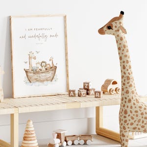May include: A framed print featuring a watercolour illustration of animals on a boat. The text "I am fearfully and wonderfully made" is printed on the print. The print is hanging on a white wall above a wooden bench. There are wooden blocks with letters on them, a wooden toy train, and a stuffed giraffe on the bench.