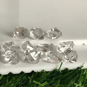 Peut inclure: Une collection de dix cristaux bruts et non taillés, transparents, aux formes géométriques irrégulières et aux surfaces à facettes. Ces pierres incolores présentent des bords naturels dentelés et des tailles variées, reflétant la lumière sur leurs structures cristallines texturées.