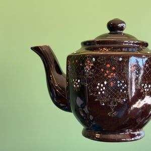 May include: A brown teapot with a floral design in gold, white, and red. The teapot has a lid and a handle.