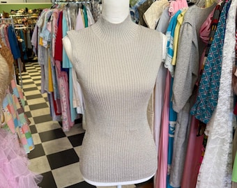 May include: A sleeveless, ribbed, beige turtleneck sweater on a white mannequin in a clothing store.