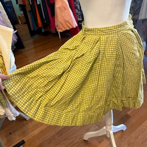 May include: A vintage-style, short skirt in a yellow and white gingham pattern. The skirt is displayed on a white mannequin and has a pleated design. The fabric appears to be cotton or a similar material. The skirt is a classic, timeless piece.