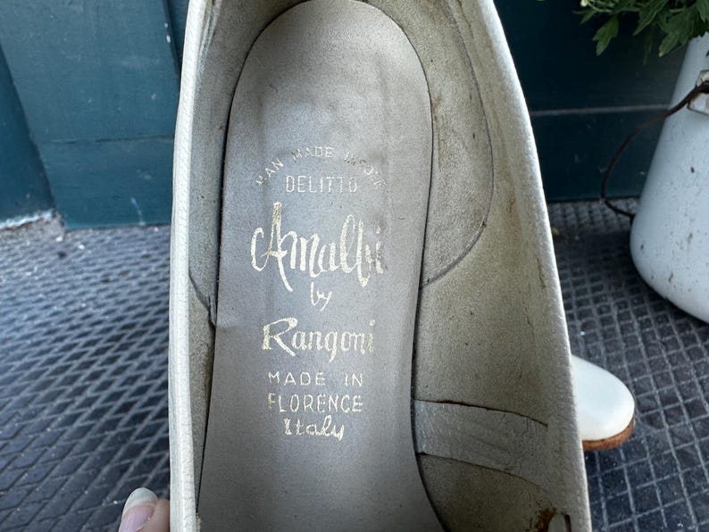 Pu&ograve; includere: Primo piano dell'interno di una scarpa bianca con il testo "Amalfi by Rangoni Made in Florence Italy" stampato sulla soletta.