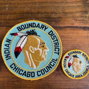 May include: Two embroidered patches with a Native American profile wearing a feathered headdress. The larger patch reads "Boundary District Indian Council Chicago" in black text on a light blue background. The smaller patch reads "Boundary District Chicago Area Council".