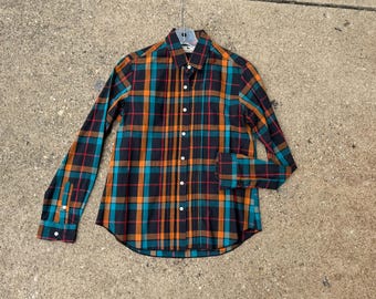 May include: A long-sleeved plaid shirt in a color palette of black, teal, orange, and red. The shirt is button-down with a collar and buttoned cuffs. The shirt is hanging on a hanger.