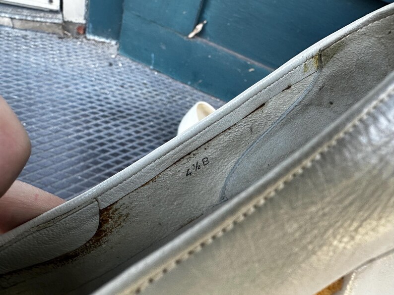 Pu&ograve; includere: Primo piano dell'interno di una scarpa di pelle bianca con la taglia 4 1/2 B stampata sulla soletta.