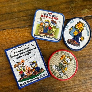 Peut inclure: Quatre écussons brodés représentant Garfield. Un écusson carré porte l'inscription 1998 CUB SCOUT DAY CAMP. Un écusson rectangulaire indique cub scout camp, because too much fun is never enough!! et Pacific Harbors Council, BSA. Deux écussons ronds.