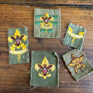 May include: A collection of five vintage Boy Scout patches. The patches are primarily green with yellow and brown embroidered details. Each patch features the Boy Scout emblem, with the words "Be Prepared" on some.