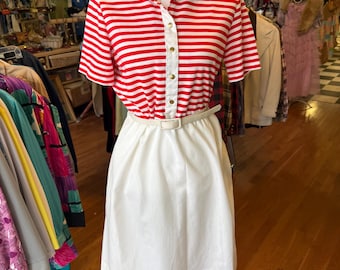 May include: A red and white striped short-sleeved shirt with a white collar and a white skirt. The shirt has a button-up front and a gold belt.