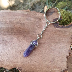 May include: A silver keyring with a purple amethyst crystal pendant. The crystal is faceted and has a pointed tip.