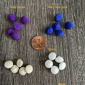 May include: Assortment of 10mm fabric covered buttons in deep purple, navy blue lapis, beige, and white. The buttons are shown next to a US penny for size comparison.