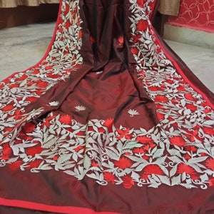 Pu&ograve; includere: Un sari di seta marrone con ricami bianchi e rossi. Il ricamo presenta motivi floreali con foglie e fiori.