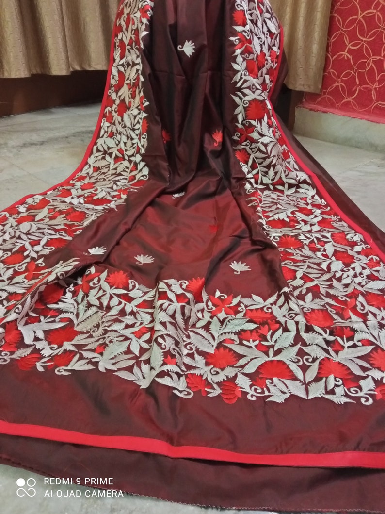 Pu&ograve; includere: Un sari di seta marrone con ricami bianchi e rossi. Il ricamo presenta motivi floreali con foglie e fiori.