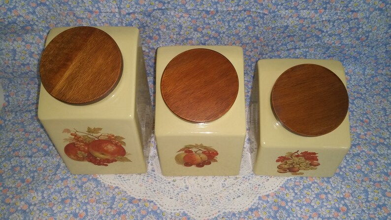 Peut inclure: Ensemble de trois pots en c&eacute;ramique avec couvercles en bois. Chaque pot pr&eacute;sente un motif de fruit diff&eacute;rent&nbsp;: des pommes, des poires et des raisins. Les pots sont de couleur jaune p&acirc;le.