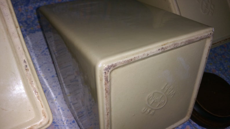 Peut inclure: Gros plan du fond d'un pot en c&eacute;ramique de couleur cr&egrave;me avec un bord brun. Le pot a un logo avec un c&oelig;ur et le texte "USA" imprim&eacute; au fond.