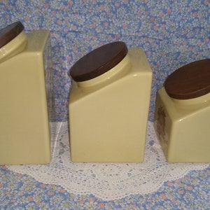 Peut inclure: Ensemble de trois pots en c&eacute;ramique avec des couvercles bruns. Les pots sont jaunes avec un motif subtil et sont dispos&eacute;s par ordre de taille d&eacute;croissante.