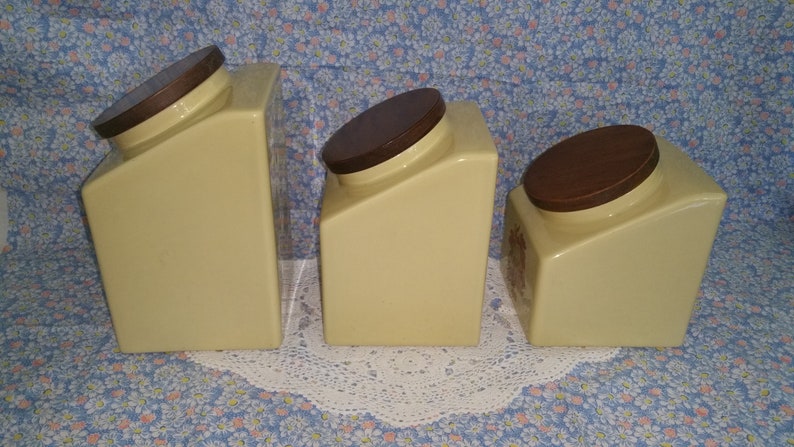 Peut inclure: Ensemble de trois pots en c&eacute;ramique avec des couvercles bruns. Les pots sont jaunes avec un motif subtil et sont dispos&eacute;s par ordre de taille d&eacute;croissante.