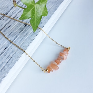 May include: A gold chain necklace with a row of small, peach-colored sunstone chips.
