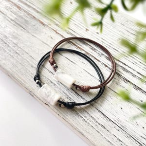 May include: Two friendship bracelets with white marble beads and brown and black cords.
