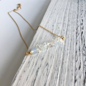 May include: A delicate gold chain necklace with a bar pendant featuring a row of small, white opal stones.