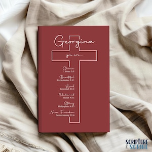 May include: A burgundy journal with a white cross and the name "Georgina" written in cursive. The cross has bible verses written on it, including "Chosen", "Beautiful", "Loved", "Redeemed", "Strong", and "Never Forsaken".