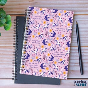 May include: A pink notebook with a floral pattern and birds in flight. The notebook features a quote from the Bible about birds and their worth. The quote reads: "Look at the birds of the air... they neither sow nor reap... and yet your heavenly Father feeds them. Are you not of more value than they?"