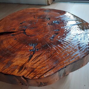 May include: A round, wooden table top with a natural, organic shape. The surface is a rich, dark brown with visible wood grain and a glossy finish. A large crack runs across the top. The table top is approximately 24 inches in diameter.